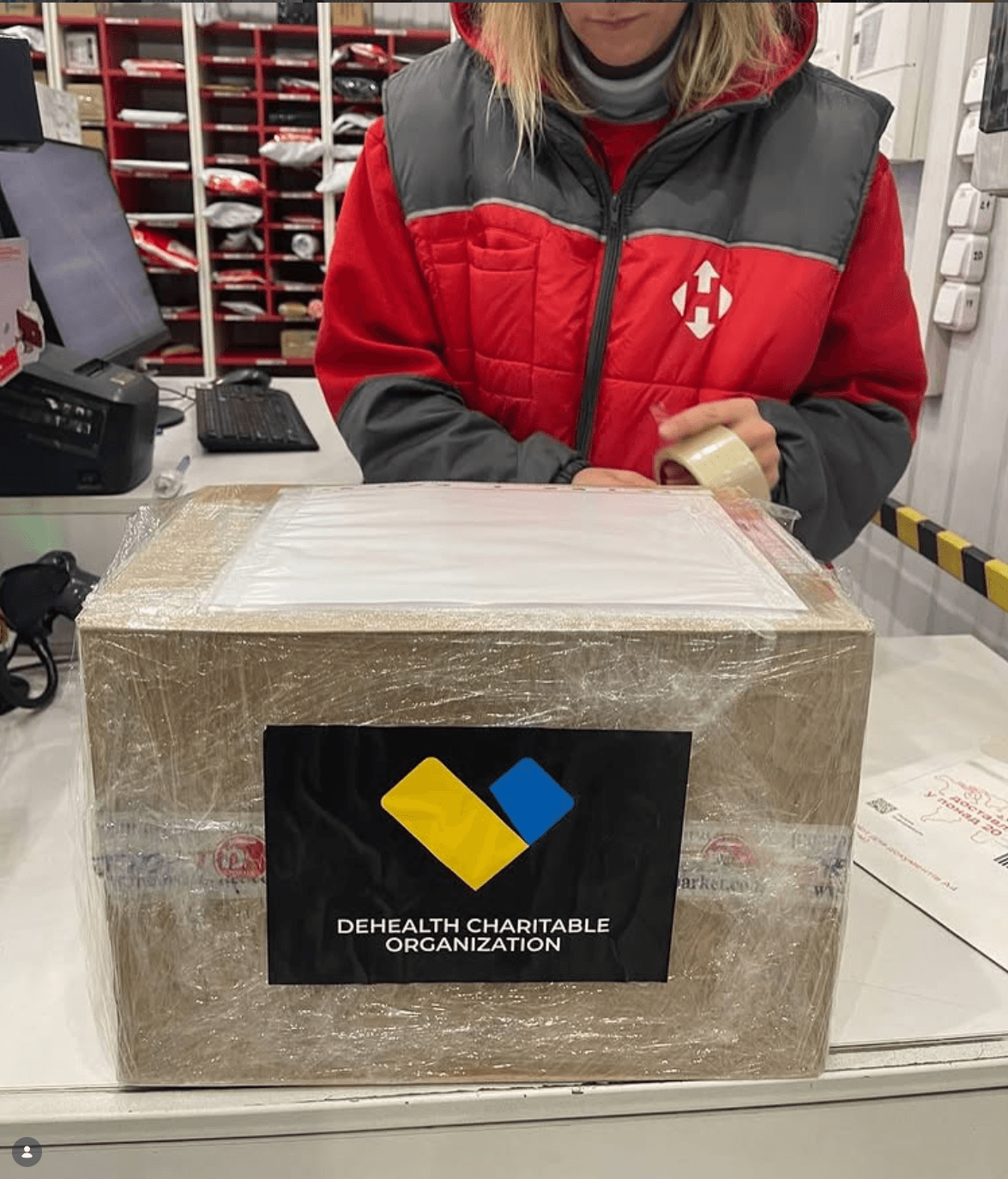 Працівниця Нової Пошти запаковує коробку медикаментів з логотипом DeHealth для відправлення